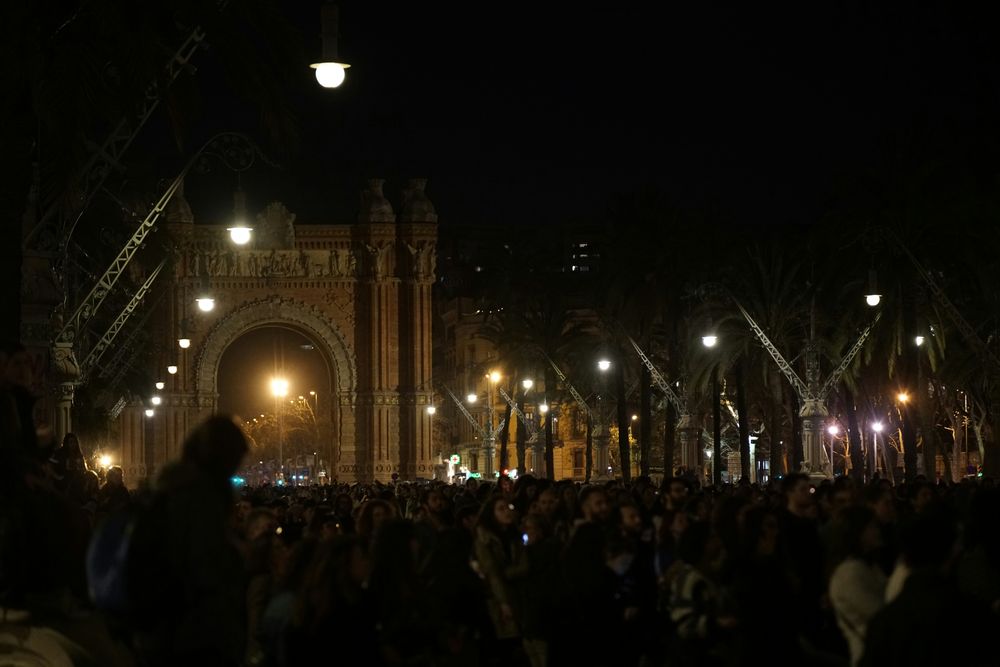 Dichte Menschenmenge bei Nacht vor dem beleuchteten Arc de Triomf in Barcelona