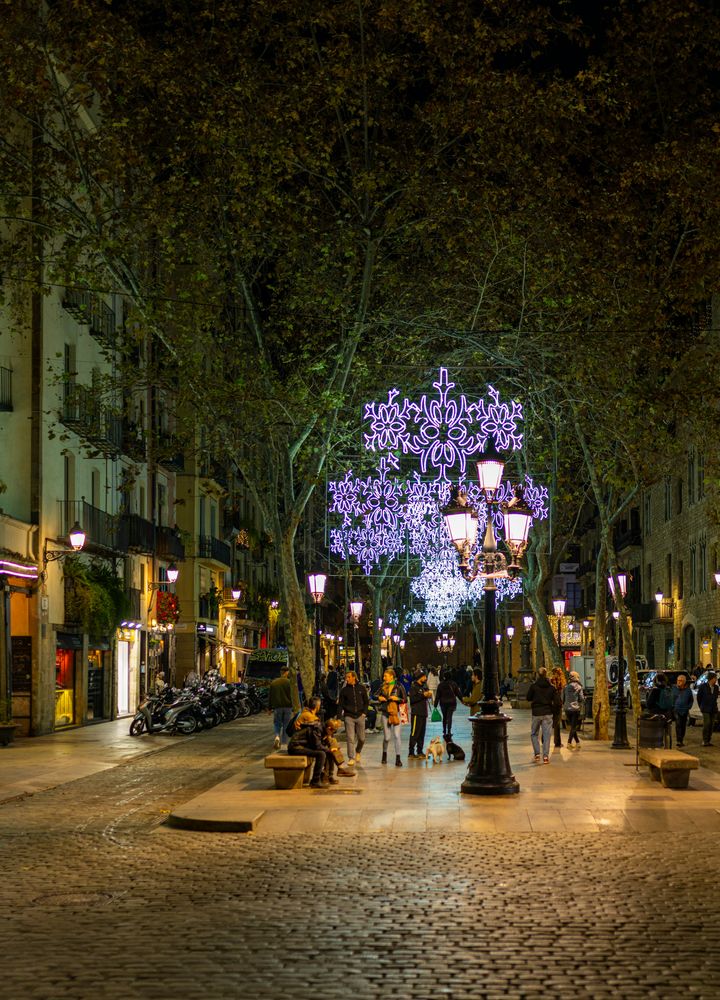 Straße in Barcelona bei Nacht mit großem Leuchtornament an einer Laterne und Passanten