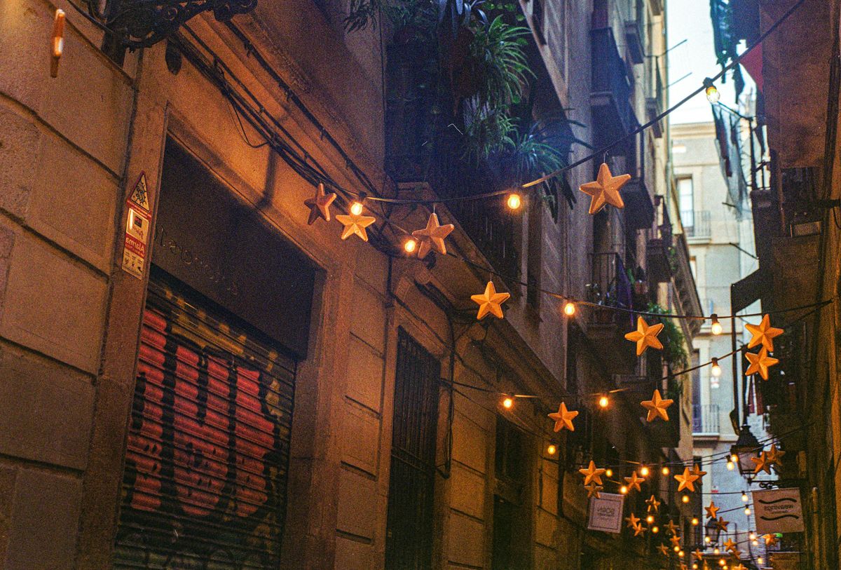 Enge Altstadtgasse in Barcelona, über der Lichterketten mit großen leuchtenden Sternen gespannt sind