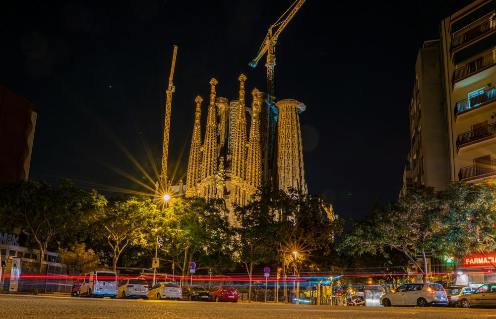Die beleuchtete Sagrada Família in Barcelona bei Nacht, davor Lichtspuren des Verkehrs