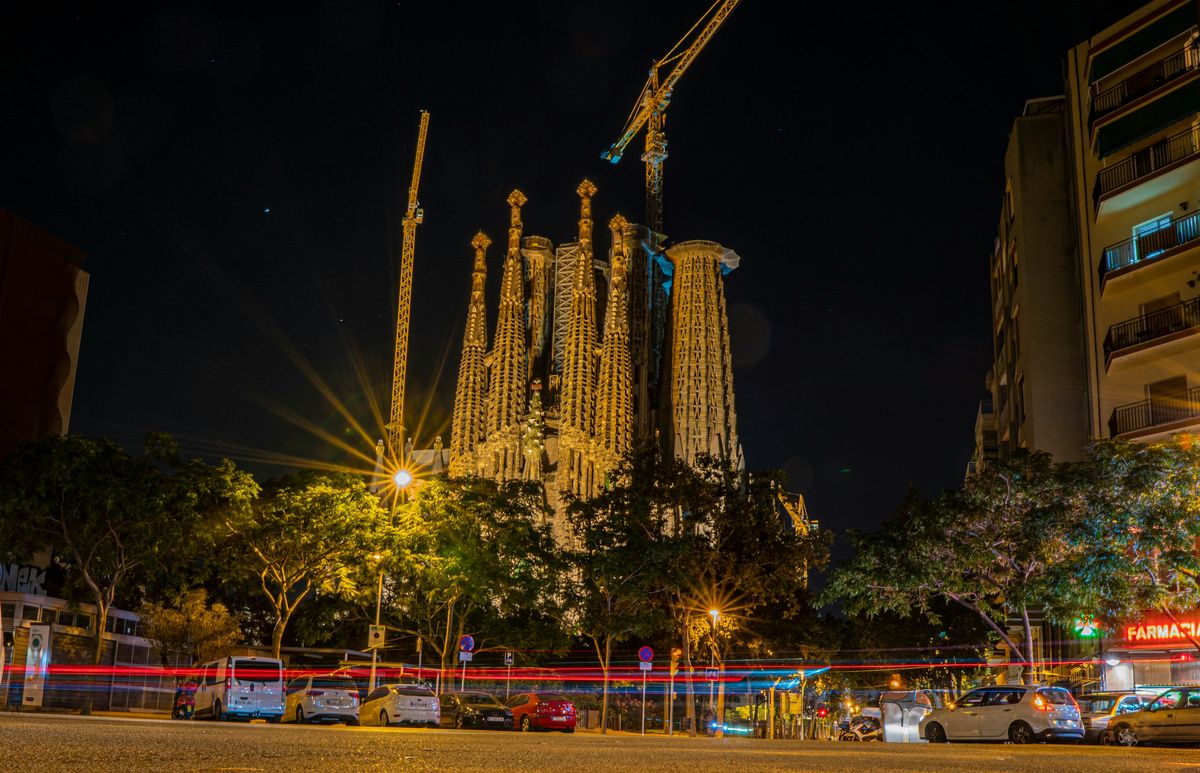Die beleuchtete Sagrada Família in Barcelona bei Nacht, davor Lichtspuren des Verkehrs