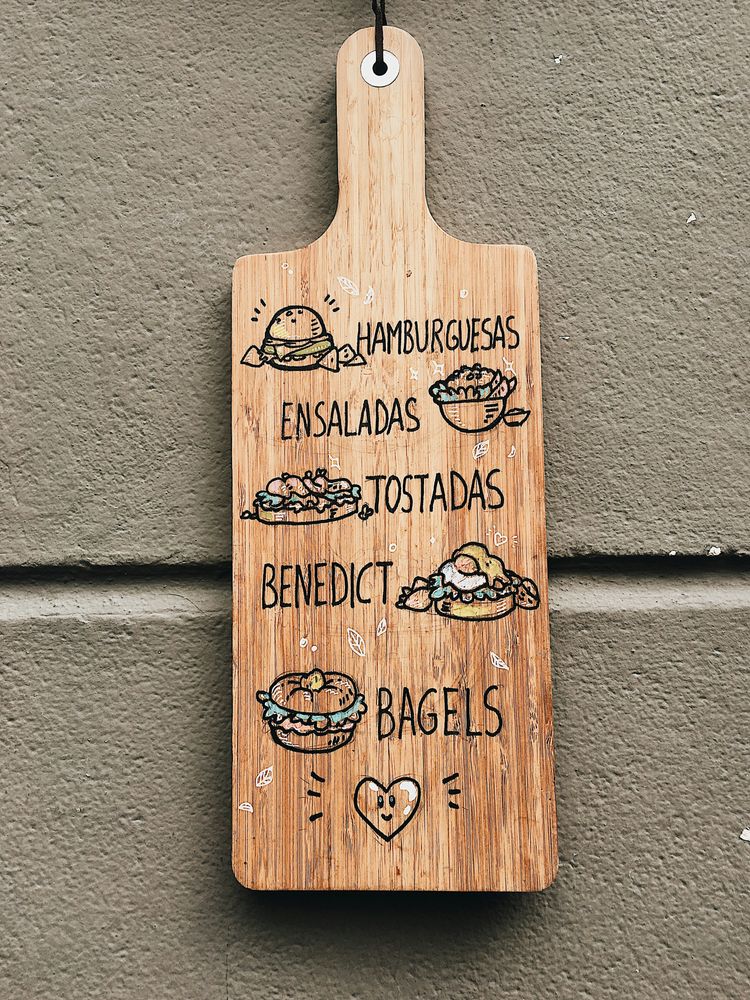 Handbeschriftetes Holzbrett als Speisekarte an einer Hauswand, mit gezeichneten Gerichten und spanischen Bezeichnungen